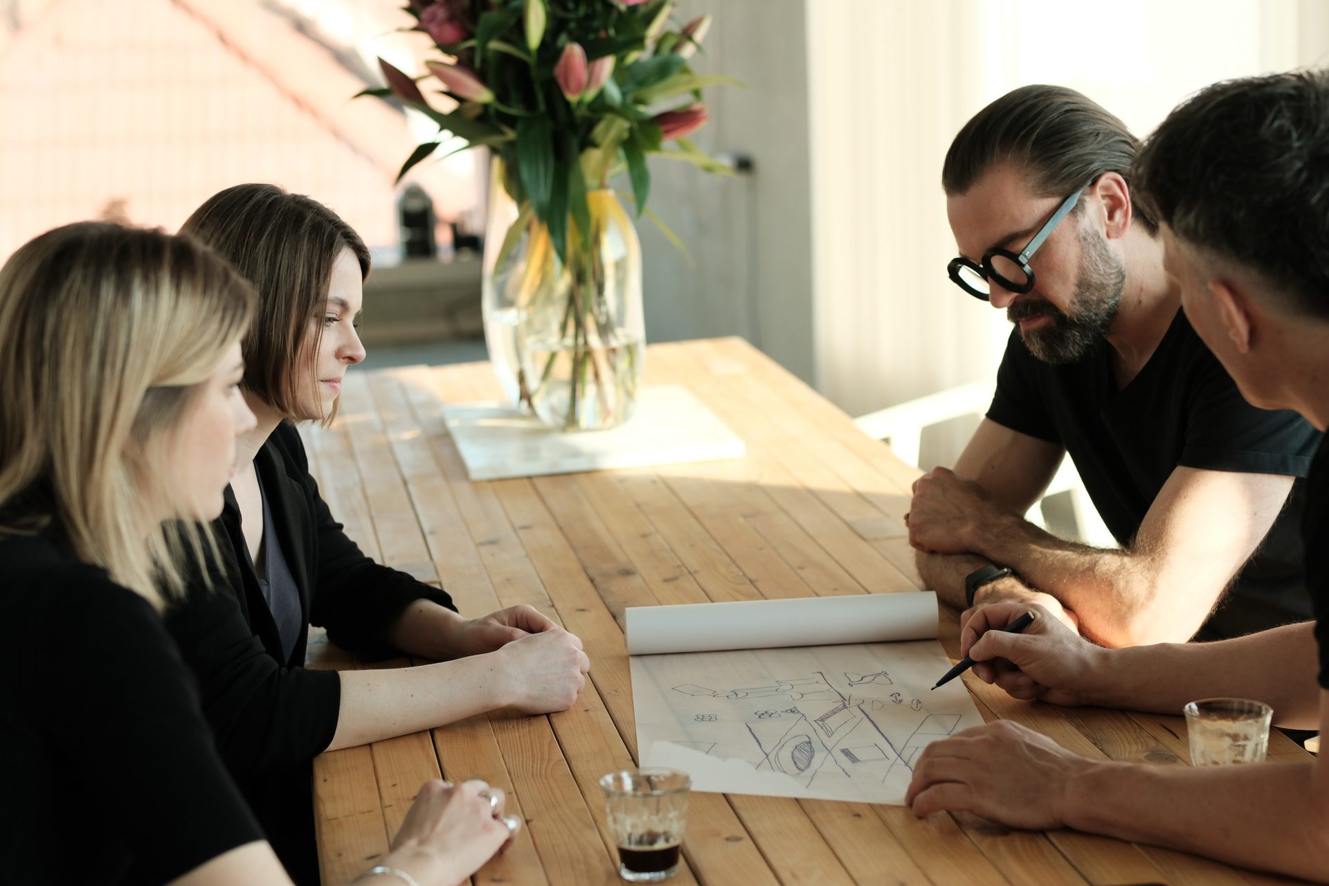 Team at the wooden table over an unrolled sketch, pen in hand