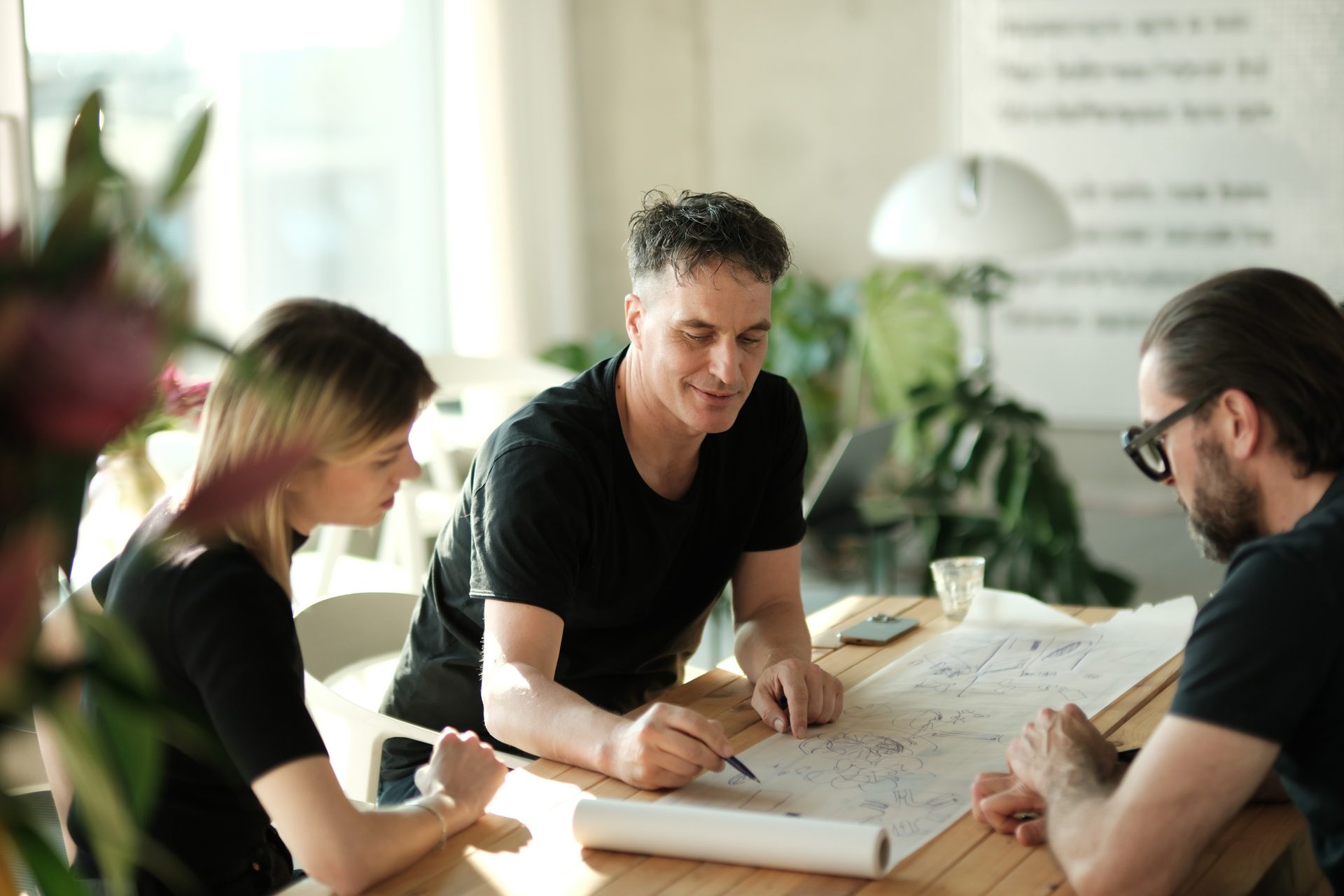 Three people drawing together on a sketch on the meeting table